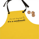 It's a Condiment Mustard Apron - Image description - an adult wearing the mustard colored yellow apron with saying It's not dog hair it's a condiment with an outline of a condiment  bottle with 3 chocolate chip cookies. The black neck time straps are attached with black buttons.